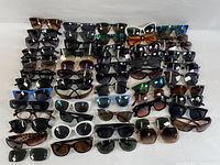 Full overview of approximately 45 pairs of assorted men’s and women’s sunglasses in various colors and styles laid out on table.