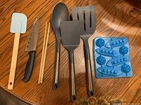 Photo showing assorted kitchen utensils and two silicone ice cube trays on round wooden surface.