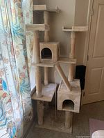 Full view of the multi-level beige cat tree showing platforms, two enclosed cubby holes, ramp, and sisal-wrapped scratching posts.