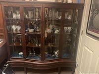 Front view of antique wooden display case showing glass doors, brass hardware, and items inside for size context