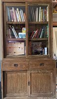 Front view of the full distressed wood cabinet with sliding glass doors filled with books and items, drawers, and lower sliding doors closed.
