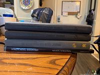 Four workout and anatomy books stacked: three workout journals with dark hardcover bindings and one stretching anatomy book with black spine.