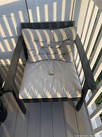 Outdoor chair with beige tufted cushions on dark weatherproof frame, showing detail of cushion and chair arm.