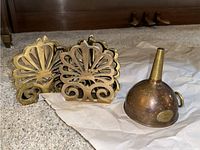Photo showing four decorative brass bookends and a brass funnel placed on a cloth on the floor.