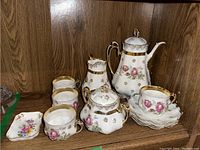 Full view of all tea set items with teapot, sugar bowl, creamer, four cups and four saucers arranged on wooden shelf