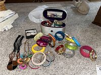 Wide view of assorted costume jewelry including numerous colorful bracelets and bangles, necklaces and earrings in an open jewelry box with mirror.