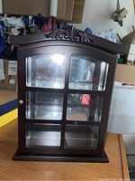 Front view of wood display cabinet showing glass panel door and carved wood top design