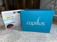 Blue Capillus retail box front and white product packaging box back displayed on floor