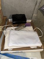 Photo showing two handbags and white laundry bag in a tray, along with a small purple box likely containing purse size perfume.