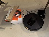 Moosoo R4 robot vacuum with charging dock, power adapter, and box containing Neato vacuum attachments on floor.