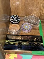 Photo showing various glass paperweights and the clear signed glass dish on wood shelf.
