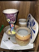 Photo showing ceramic goblet with colorful hand-painted design, two stoneware vases, signed bowl, signed ceramic platter, and pottery trivet all arranged on a white tray