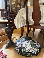 Side view of the metal base and stained glass shade placed on the floor near wooden furniture.