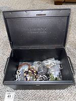 Open metal box labeled 'Hefix' showing various jewelry items packed inside plastic bags.
