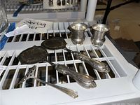 Three sterling silver serving utensils (two spoons and one fork) and two sterling silver bud vases on a white rack.