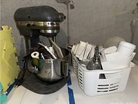 Front angled view of vintage KitchenAid mixer with stainless steel bowl filled with various attachments and a basket containing additional parts