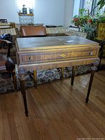 Front view of antique wooden desk showing rectangular top, inlaid drawer front and carved legs.