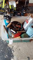 Plastic bin filled with assorted yard and garden tools, gloves, string rolls, and fabric.
