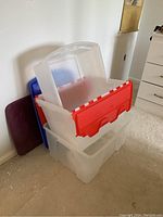 Three large translucent plastic storage bins stacked together, visible red, blue, and burgundy lids.