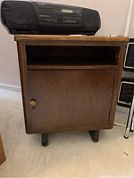 Front view of the vintage wood console cabinet with the door closed and a radio on top.