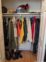 Closet with various men's and women's jackets, coats, and boots arranged on hangers and floor
