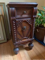 Front and side view of the vintage wooden end table cabinet showing ornate carvings, one drawer with metal knob, and a cabinet door with ring pull.