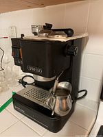 Overall view of the Black & Decker espresso machine with milk frother pitcher on drip tray, showing the machine's front and side with portafilter on top.