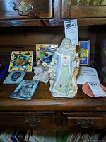 Front view of lot showing Old World St. Nicholas figurine in pastel colors with surrounding art tiles and plaques on wooden shelf.