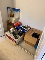 Wide view of the lot showing stacked reams of printer paper in plastic, cardboard boxes, some office supplies visible on top of a large Xerox box on the floor.