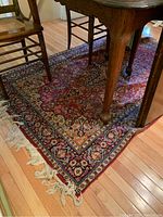 Full view of the vintage oriental rug under wooden furniture showing detailed patterns with a red field and multicolor floral border.