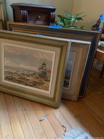 Three framed coastal paintings leaning against wall on hardwood floor