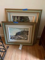 Two framed paintings stacked against wall showing both frames