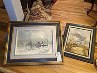 Two framed paintings signed by Bruce Le Dain shown side by side, one larger winter barn scene and one smaller farm scene with cornstalks.
