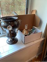 Cardboard box of silverware next to trophy cup on windowsill
