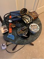 Overview photo showing all items on a small round table including bolo ties, watches, trinket boxes, business card holder, and jewelry.