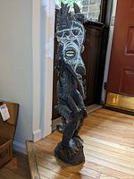 Full side view of the tall wooden tribal figure with painted white and brown markings and carved details