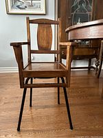 Front view of altered wooden high chair with armrests mounted on metal legs, medium brown wood and black metal, with removable seat pad included.