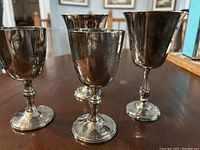 Four silver plate goblet wine chalices displayed on a wood table showing their shape and finish. Classic rounded bowl with slender stems and round bases.