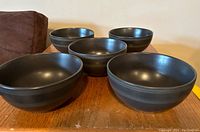 Five black bowls displayed on a wooden surface, showing the overall set.
