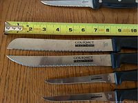 Photo showing multiple Gourmet Traditions knives next to a tape measure indicating blade lengths from 2 to 8 inches