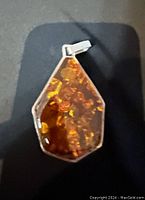 Close-up of the amber pendant showing natural amber inclusions and silver-tone loop.