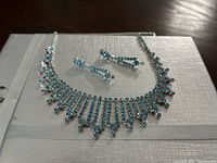 Aqua crystal necklace and earrings displayed on a white textured surface showing the sparkle and design.