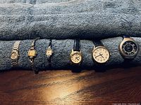 Collection of six watches laid out on a dark grey textured surface showing full watches from face to strap.