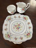 View of square cookie plate, creamer, and sugar bowl showing floral and gold rim details.