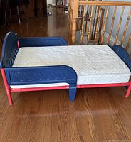 Side view of Delta toddler bed with blue plastic headboard and footboard, red steel frame, white mattress on top