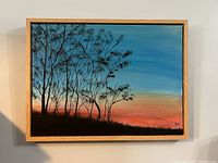 Frontal view of acrylic painting showing tree silhouettes against a colorful evening sky with a natural wood frame.