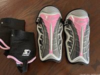Photo of the front side of pair of girls Starter soccer shin guards in black, gray, and pink, shown with ankle guards on a wooden surface