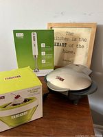 Shows Zoku Ice Cream Maker box and unit, TRU immersion blender box, GT Express 101 maker, and framed kitchen sign