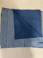 Folded medium blue denim fabric showing layered edges and double-sided color tones.