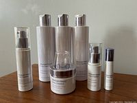Seven-piece set of Meaningful Beauty skincare products by Cindy Crawford arranged on table: includes three identical tall white bottles with silver caps (pore refining toners), pump bottles, and a jar.